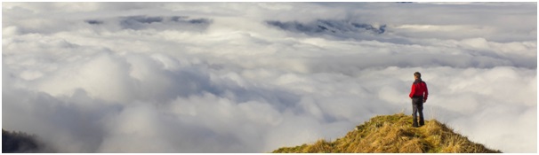 Man on mountain top looking across cloud covered landscape, illustrating the fact that completing one's application is only the first step in the journey to landing a consulting job