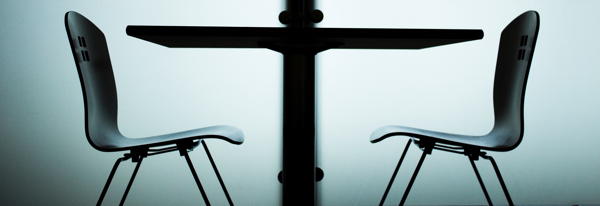 two empty office chairs facing one another with a desk in between