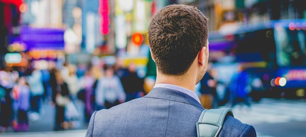 Businessman in blue suit with satchel viewed from behind looking into busy city