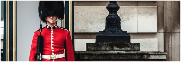 British Army Guardsman in red dress uniform and black busby standing guard at a Royal palace