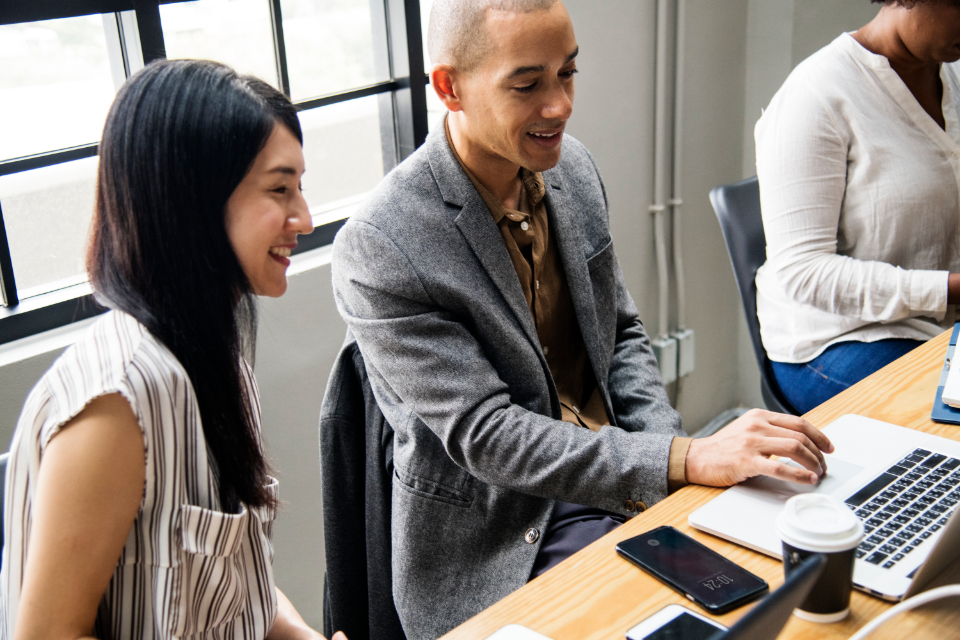 Men and women at a desk in an office working on laptops