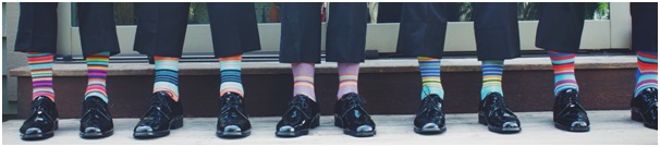 Row of men in dark suits and black shoes hoisting their trousers to reveal brightly striped socks